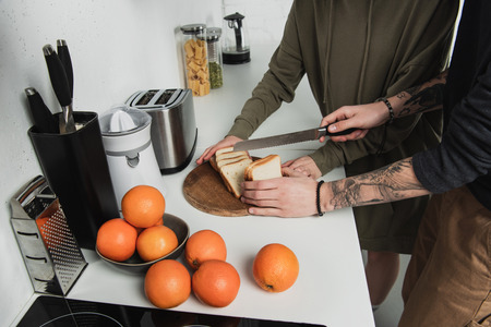 cropped view of couple preparing breakfast and cutting bread in kitchenの写真素材