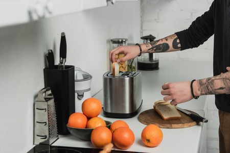 cropped view of tattooed man preparing toasts with toaster during breakfast in kitchenの写真素材