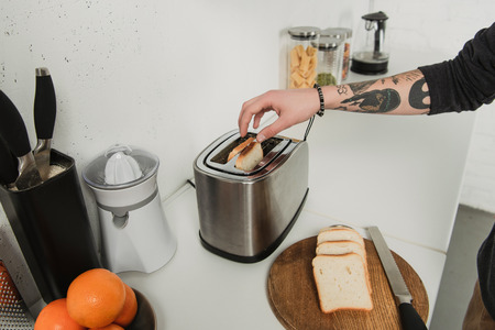 cropped view of tattooed man preparing toasts with toaster during breakfast in kitchenの写真素材