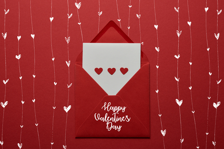 top view of Happy valentines day lettering with hearts in envelope on red background