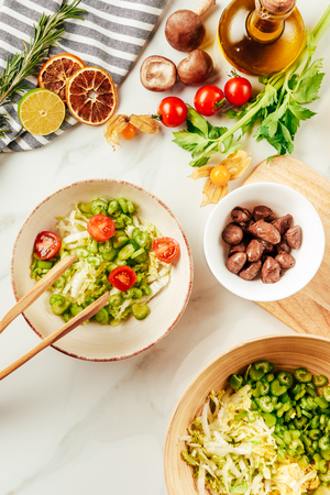 top view of salad on white bowl with bottle of oil, cherry tomatoes, lime and rosemary on surfaceの写真素材