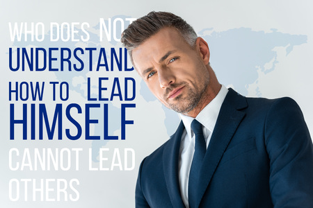 low angle view of handsome businessman looking at camera isolated on white with "who does not understand how to lead himself cannot lead others" letteringの写真素材