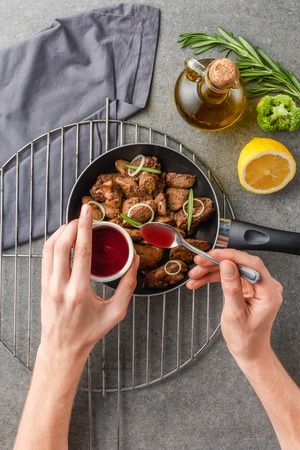 cropped view of woman adding souce in fried meat with oil, broccoli and lemonの写真素材
