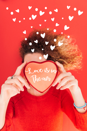top view of girl holding heart symbol with "love is in the air" lettering in front of face isolated on red, st valentines day conceptの写真素材