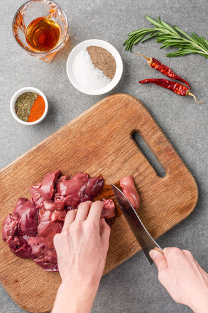 cropped view of woman cutting raw meat on cutting board among spices, glass of cognac, peppers and rosemaryの写真素材