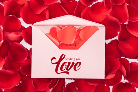 top view of envelope with sending you love lettering, heart shaped confetti and red rose petals on...
