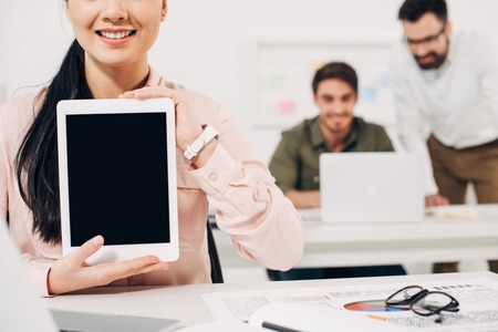 Cropped view of woman holding digital tablet with blank screen in officeの写真素材
