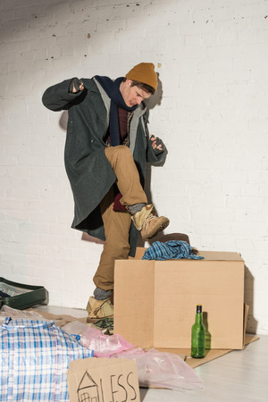 homeless man aggressively pushing rubbish into box by kickingの写真素材