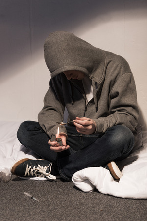 addict man seating on bedding and heating spoon with heroin on lighterの写真素材