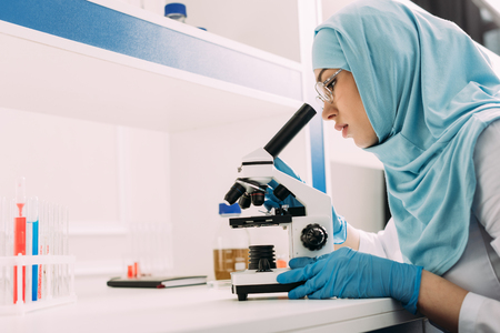 female muslim scientist looking through microscope during experiment in chemical laboratory with copy spaceの写真素材