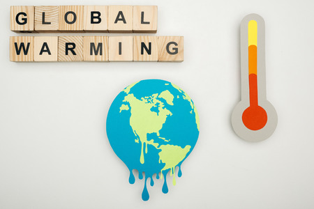 paper cut melting earth, wooden cubes with "global warming" lettering, and thermometer with hign temperature indication on scale on grey backgroundの写真素材