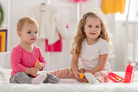adorable sisters playing with first aid kit in children room and looking at camera