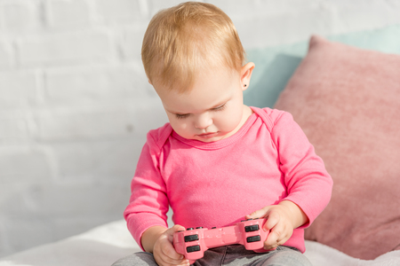 adorable kid in pink shirt holding pink joystick on bed in children roomの写真素材