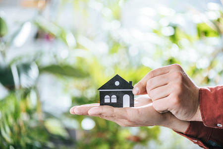 cropped view of man holding paper house in hands, energy efficiency at home conceptの写真素材