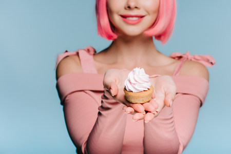cropped view of smiling girl holding sweet cupcake isolated on blueの写真素材