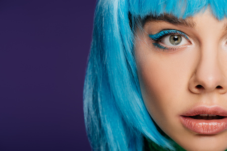 cropped view of attractive girl with blue makeup posing in blue wig, isolated on purpleの写真素材