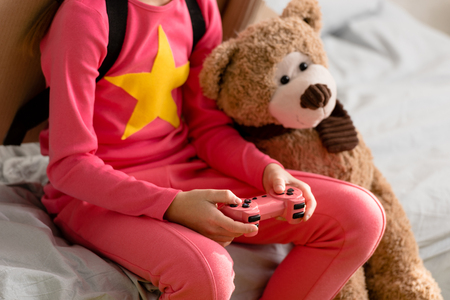 Partial view of kid with teddy bear holding gamepad