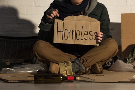 cropped view of homeless man holding piece of cardboard with "homeless" handwritten inscriptionの写真素材