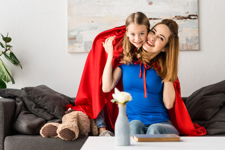 Smiling mother and cute kid in red cloaks looking at cameraの写真素材