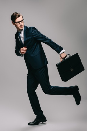 confident businessman in suit running with briefcase on grey backgroundの写真素材