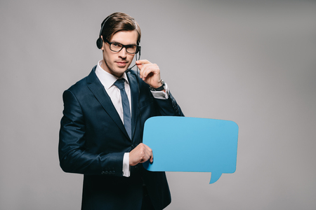 serious man in suit wearing headset and holding speech bubble on grey backgroundの写真素材