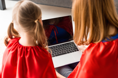 Back view of mother and daughter in red cloaks looking at laptop screenの写真素材