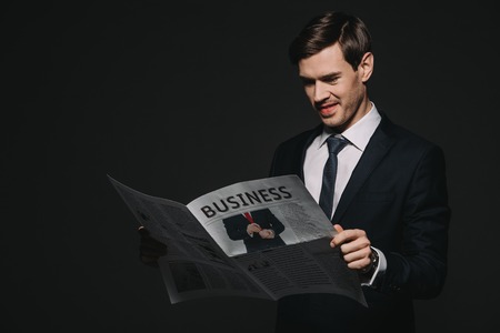 cheerful businessman reading business newspaper isolated on blackの写真素材