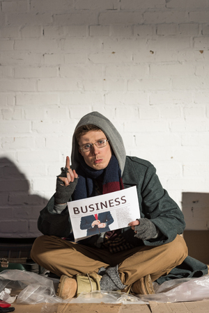 surprised homeless man holding business newspaper and showing idea signの写真素材