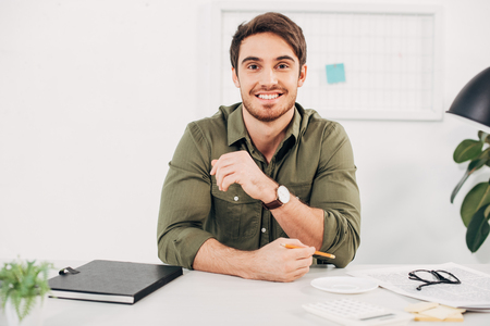 Young businessman holding pencil and smiling in modern officeの写真素材