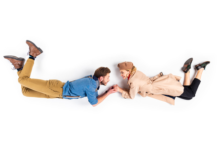 Blissful couple in casual clothes holding hands and looking at each other on white backgroundの写真素材