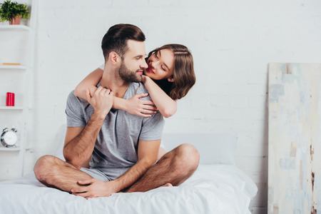 adult couple hugging and sitting on bed with white beddingの写真素材