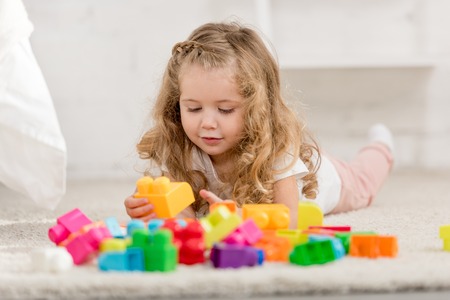 surface level of adorable kid playing with colored plastic constructor on carpet in children roomの写真素材