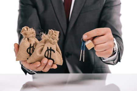 cropped view of mortgage broker holding keys and moneybags isolated on whiteの写真素材