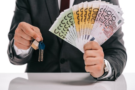 cropped view of businessman holding keys and euro banknotes isolated on white, mortgage concept