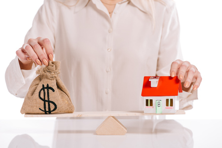 cropped view of businesswoman weighing house model and moneybag isolated on white, mortgage conceptの写真素材