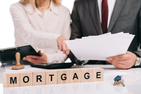 selective focus of wooden cubes with words and house model with businesspeople on background, mortgage conceptの写真素材