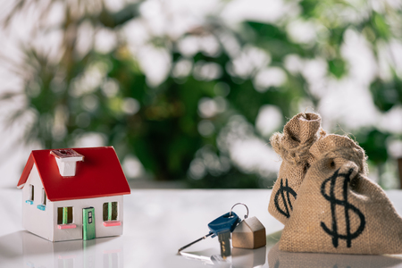 selective focus of keys, house model and moneybags with dollar signs on white desk, mortgage conceptの写真素材
