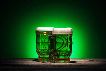 glasses of irish beer standing on wooden table on green backgroundの写真素材