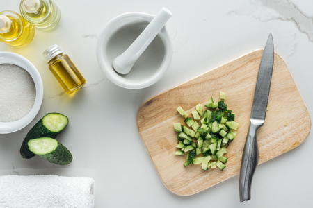 top with of wooden cutting desk with cut cucumber cubes, pounder and different ingredients for cosmetics making on white surfaceの写真素材