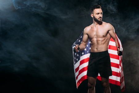 handsome shortless man holding american flag on black with smokeの写真素材