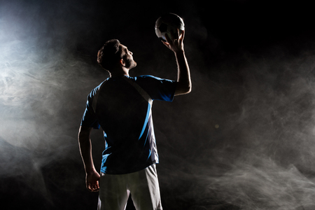 silhouette of player in uniform holding ball above head on black with smokeの写真素材