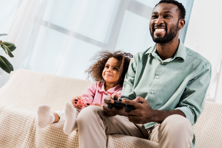 african american man and daughter playing with play stations in living room