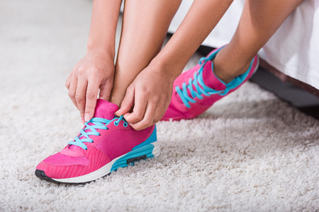 low section of sportswoman tying shoelaces on sneakers in bedroom at homeの写真素材