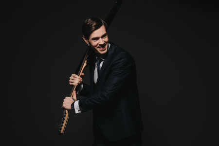 cheerful businessman holding electronic guitar in hands isolated on blackの写真素材