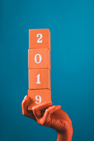 partial view of woman holding coral wooden cubes with 2019 numbers on blue background, color of 2019 conceptの写真素材