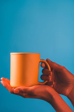 cropped view of woman holding coral coffee cup on blue background, color of 2019 conceptの写真素材