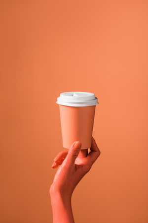 partial view of female hand with coral paper cup on coral background, color of 2019 conceptの写真素材