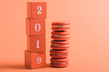 stack of wooden cubes with 2019 numbers and macarons on coral background, color of 2019 concept