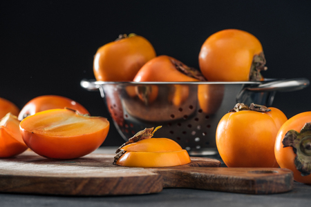 selective focus of orange persimmons on cutting board and in colanderの写真素材