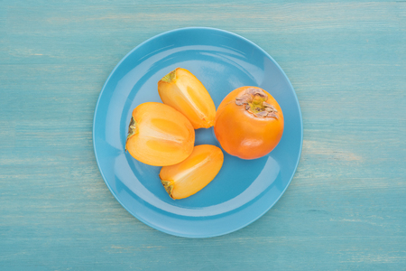top view of cut and whole ripe persimmons on blue glass plateの写真素材